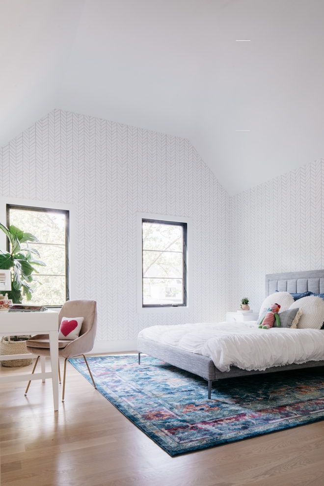 bedroom with neutral wallpaper, colored rug, bed, and desk. 