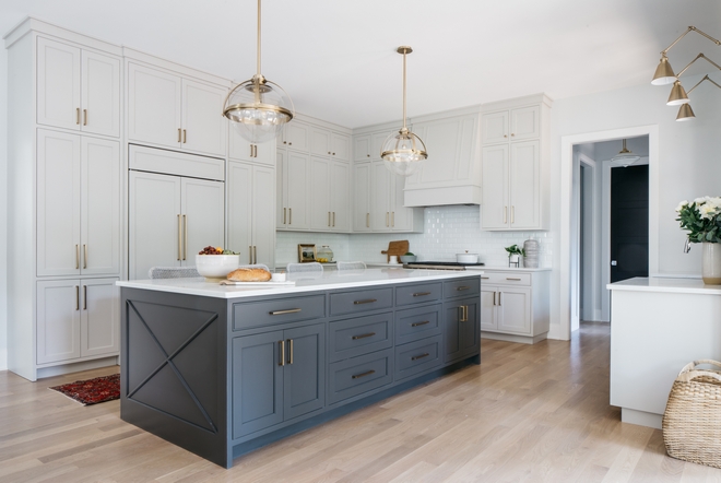 Light gray kitchen cabinets with a dark gray island. Globe lights and wood flooring.