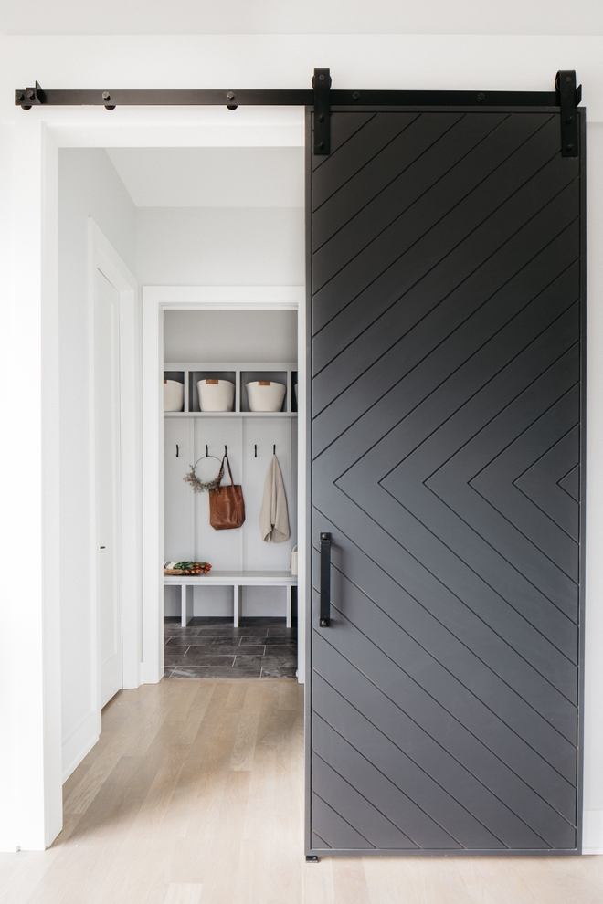 black chevron sliding barn door leading to a white painted hallway. wood floors.