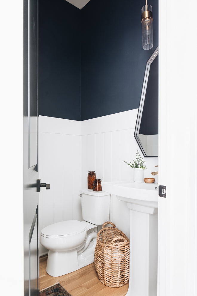 powder bathroom with white shiplap, navy accent upper wall paint, and white oak flooring. White ceramic sink with geometric mirror. 