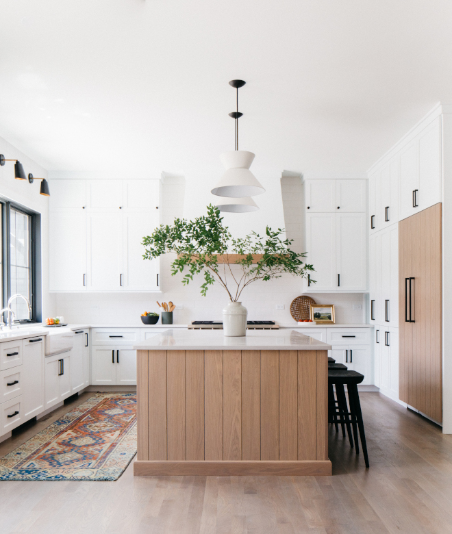 kitchen with shiplap fridge and island and farmhouse style white cabinets with black hardware. 