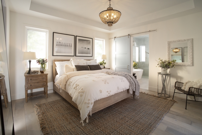 master bedroom with a dark woven rug, double windows, a sliding farmhouse style barn door, and corner accent chairs