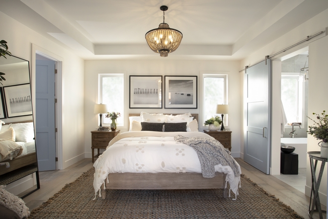 elegant farmhouse style master bedroom with a dark woven rug, double windows, a sliding barn door, and accent nightstand tables. 