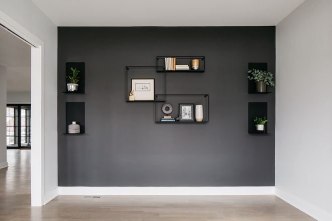 White study with a dark gray accent wall with shelves and decor