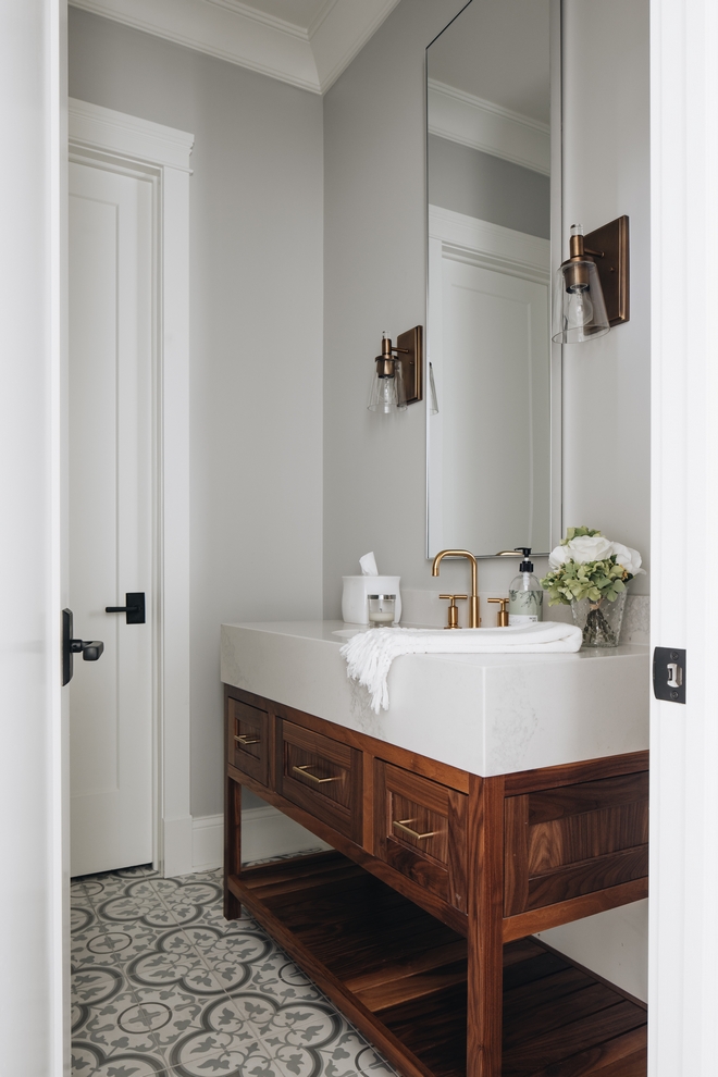 Elegant guest bathroom with gray and while swirled tile floor, chestnut vanity, and thick white counter. Bronze pulls and faucet.