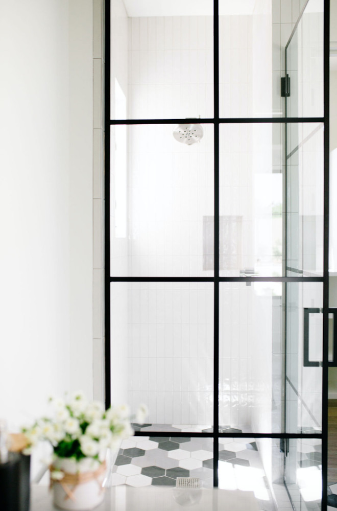 Glass encased shower with black, white, and gray hexagonal floor tiling.