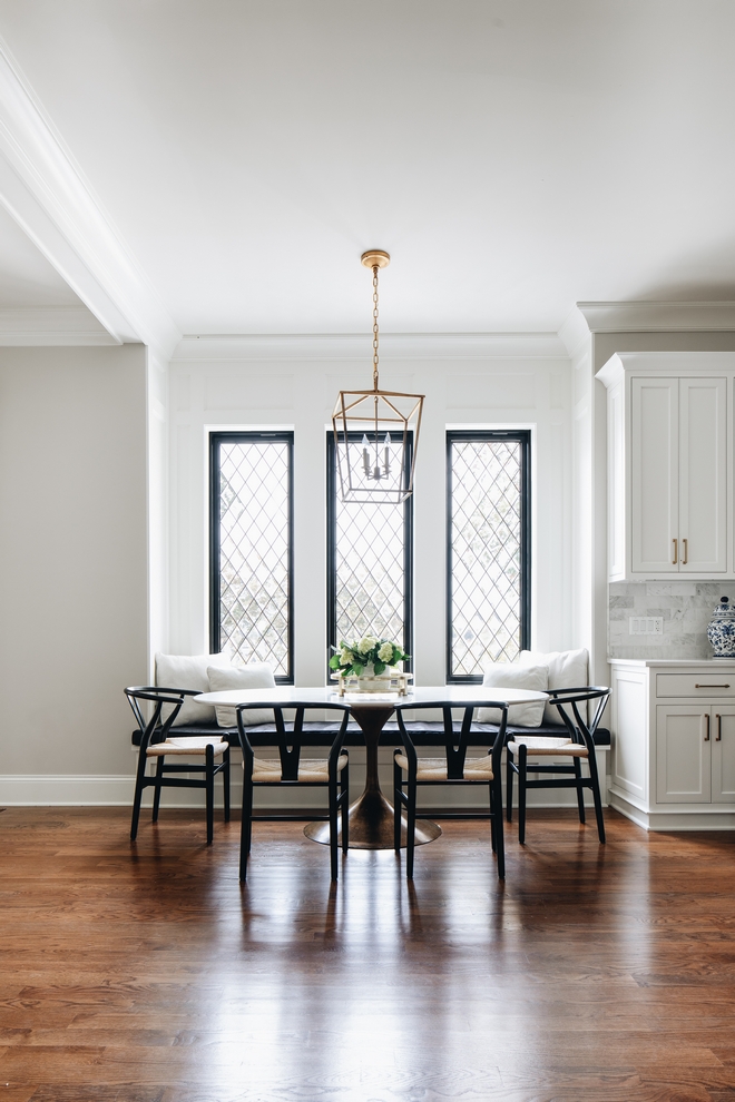 dining nook adjacent to kitchen with white round table, short black chairs, and window seat under three classic southern style latticed windows and a lantern shaped pendant.