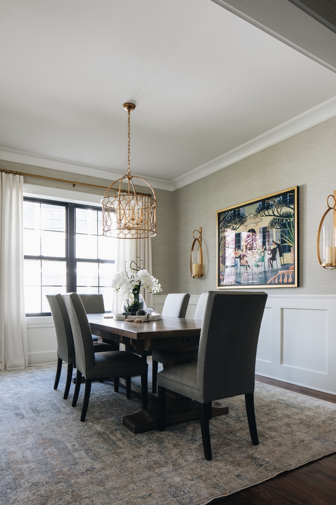 Dining room with gold accent pendant and wall lights. Dark wood table with gray leather chairs. A large window and southern-history style painting on the wall