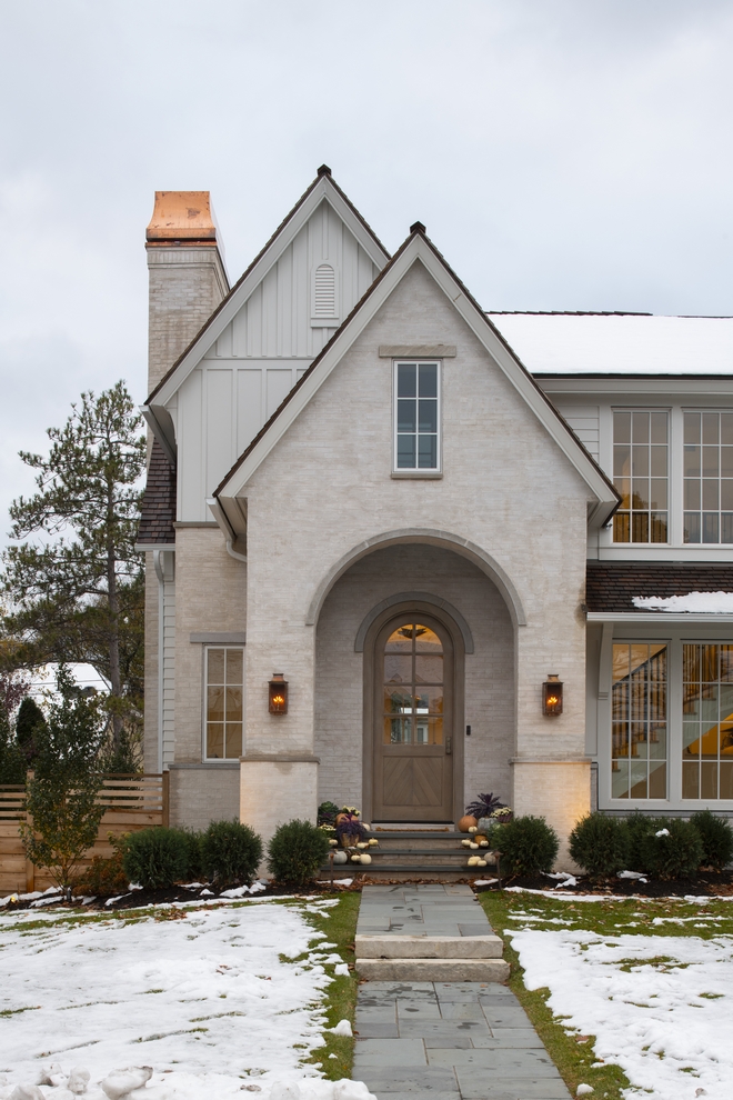 Front of european style light stone home with arched porch and doorway, white siding.