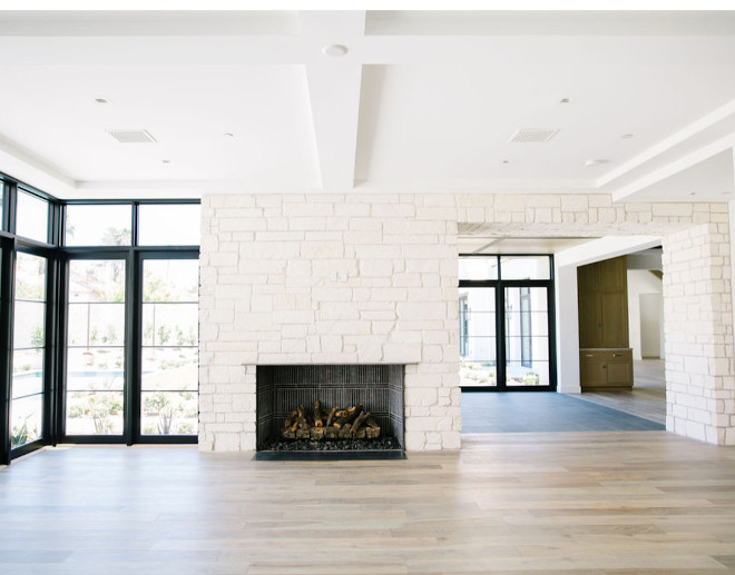 Family room with wall to wall and floor to ceiling windows, and a limestone framed fireplace. View into a breakfast room one room over
