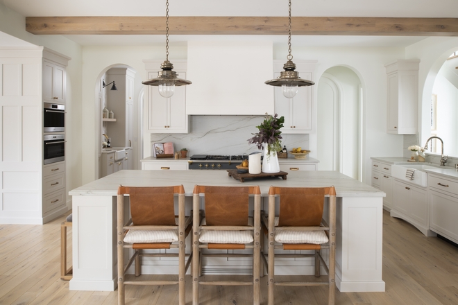 Kitchen with white cabinets and counters, leather accent chairs, exposed bulb pendant lights and arched doorways