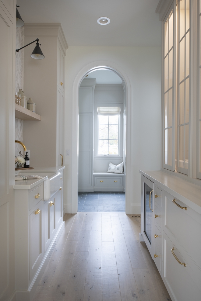 butlers pantry with tall arched doorway, interior lit glass paned cabinets, white cabinets and brass pulls. 
